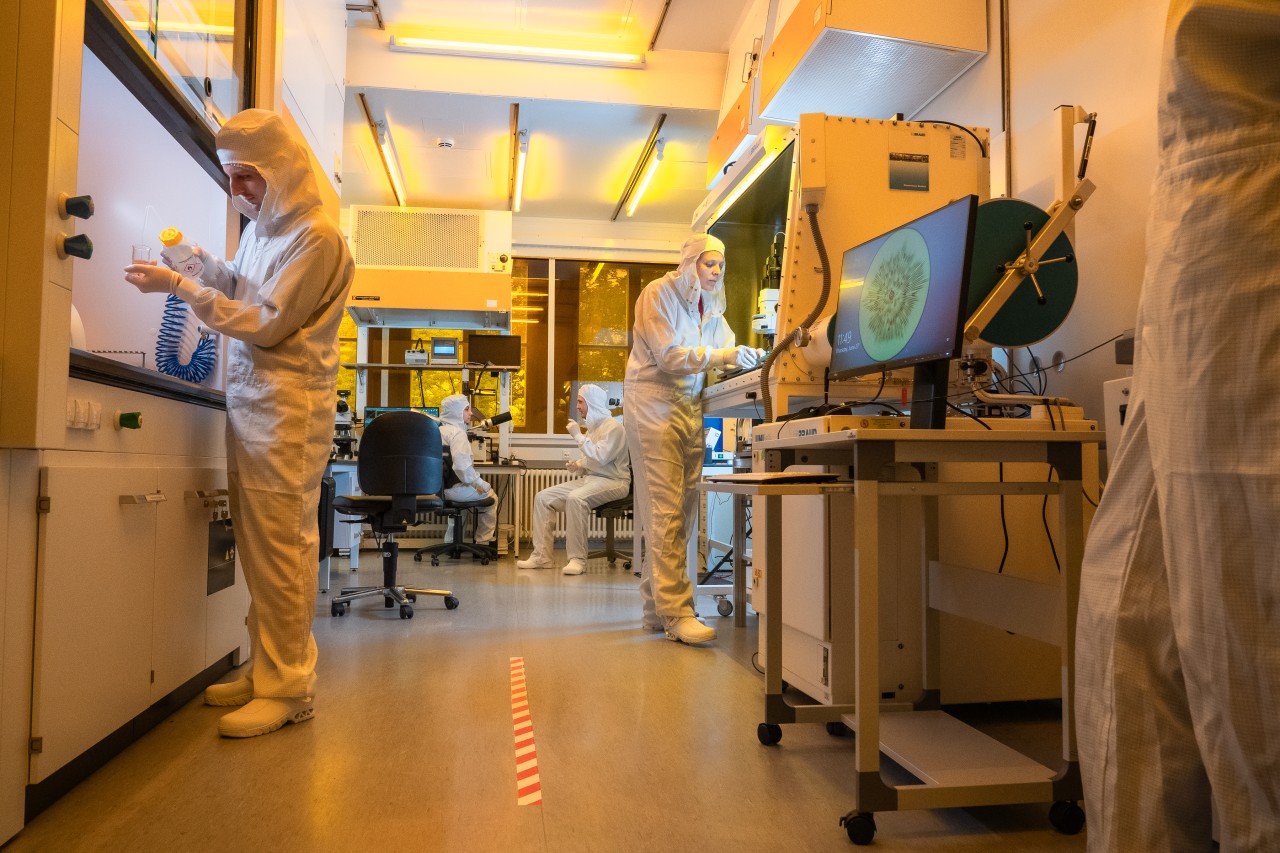 Researchers in full white suits working in a clean room laboratory.