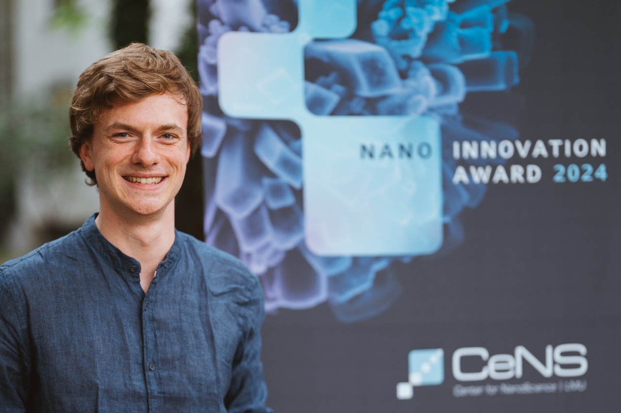 Researcher smiling and holing a Nano Innovation Award made of wood. 